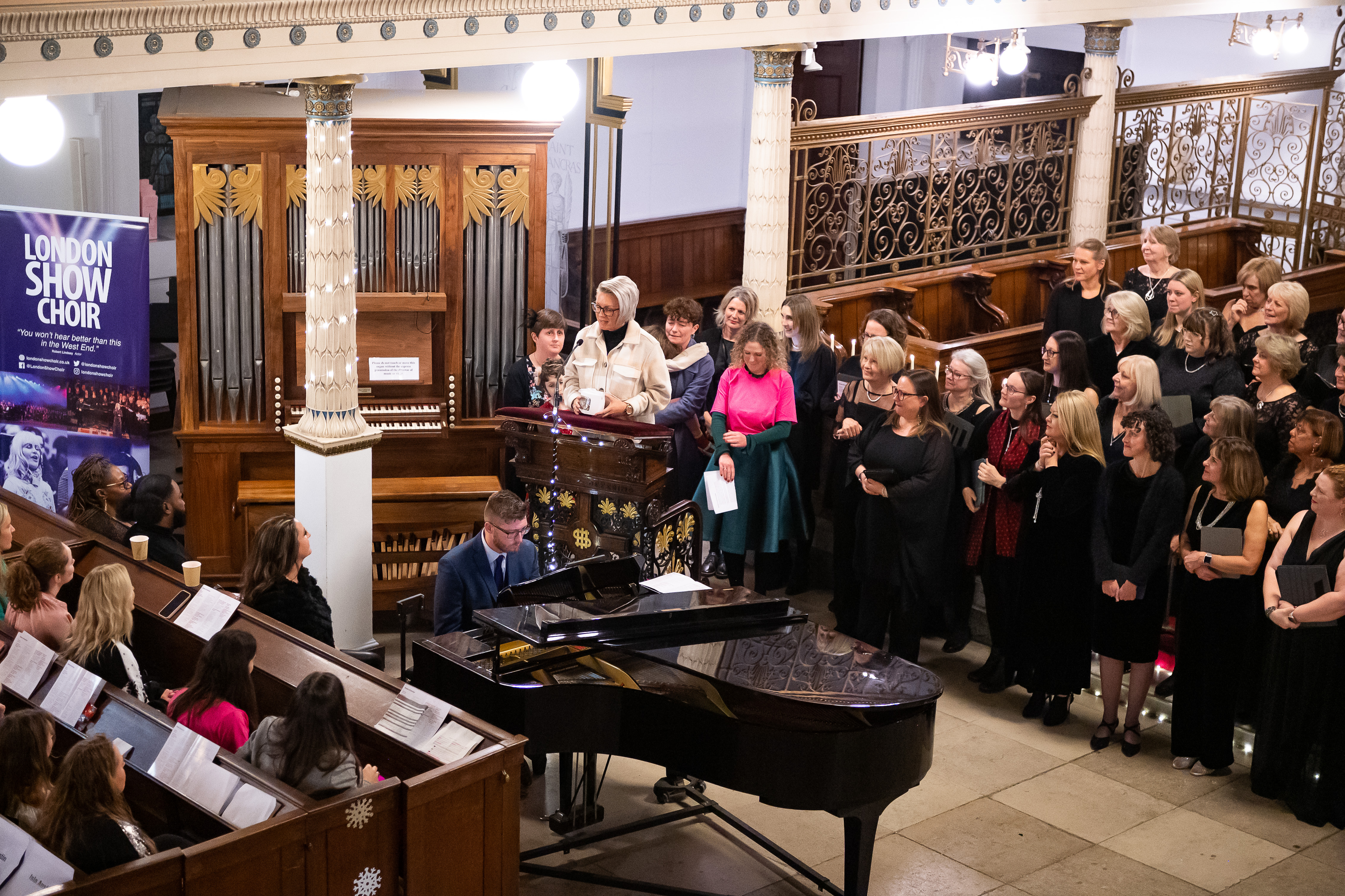 A busy carol concert with Stacey stood at a lecturn giving a speech.